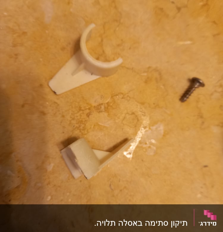 תושבת פלסטיק שבורה וברגי מתכת על רצפה